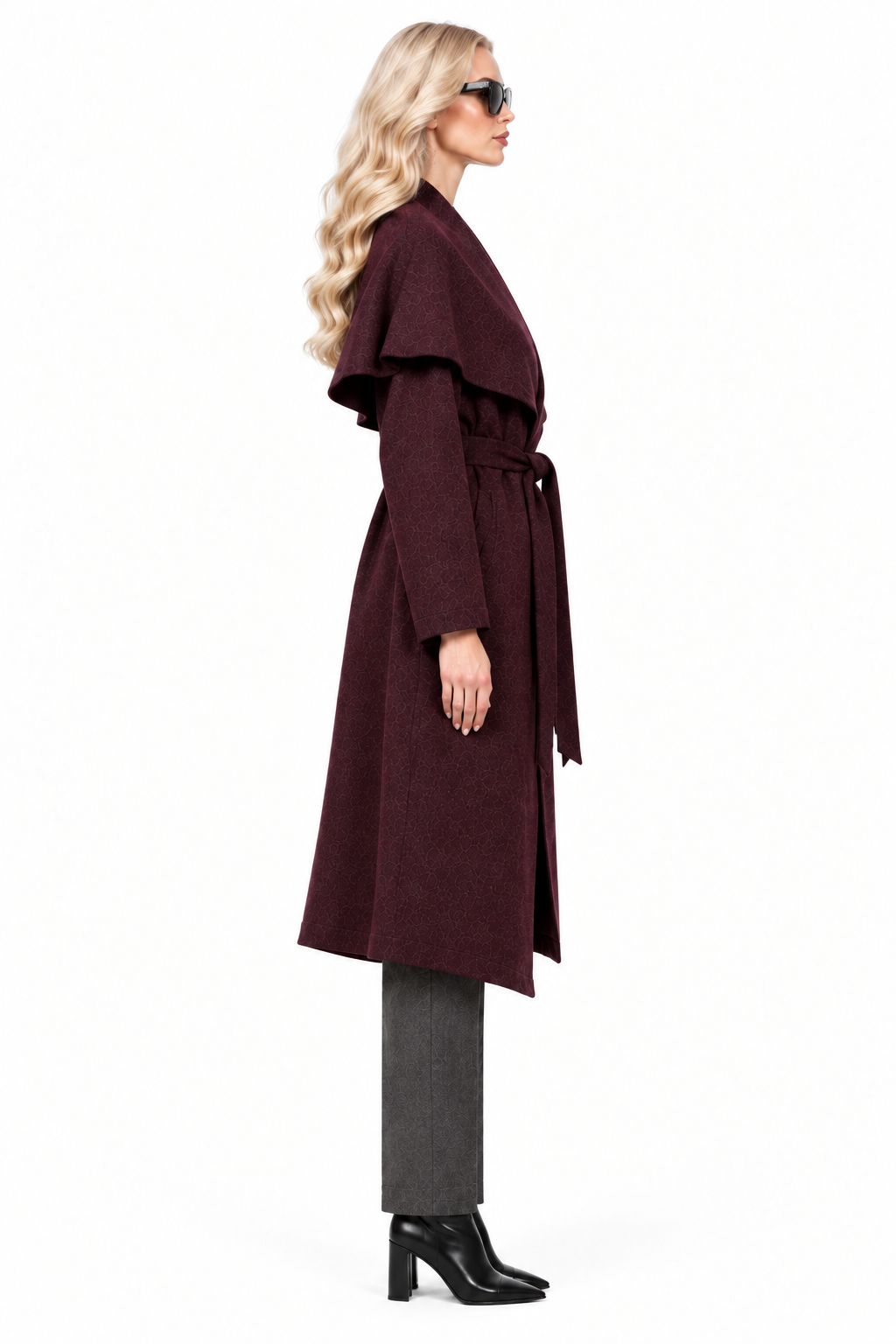 Blonde model in burgundy shawl collar long coat, charcoal trousers and black ankle boots, side view