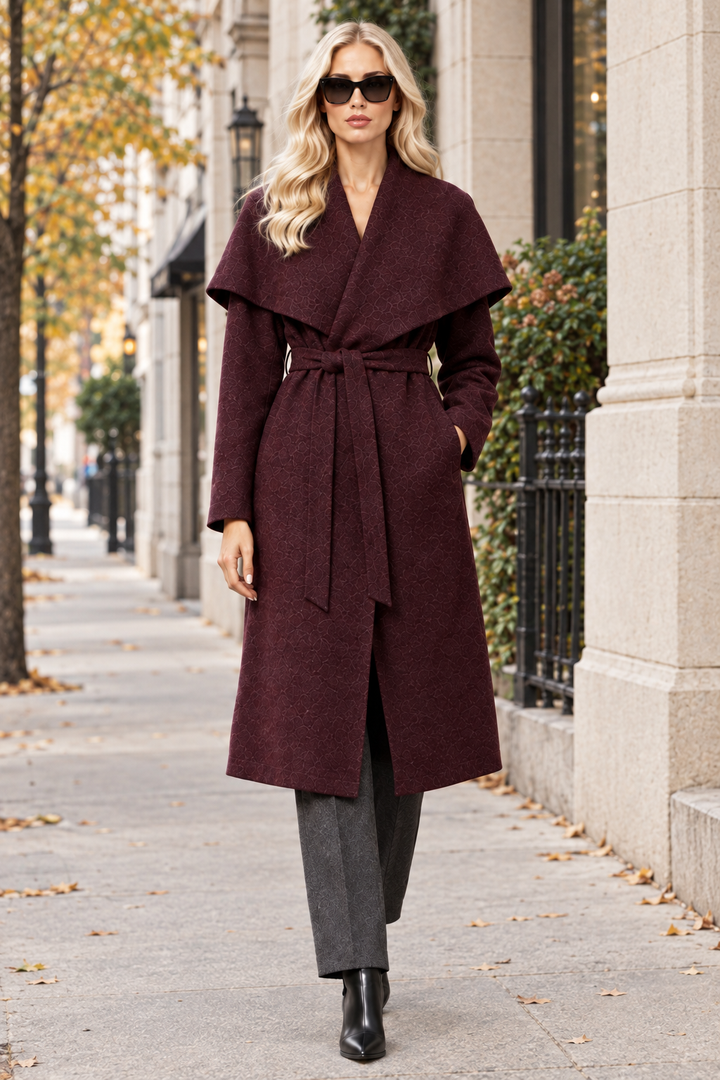 Blonde model wearing burgundy shawl collar long coat with charcoal trousers and black ankle boots on city sidewalk
