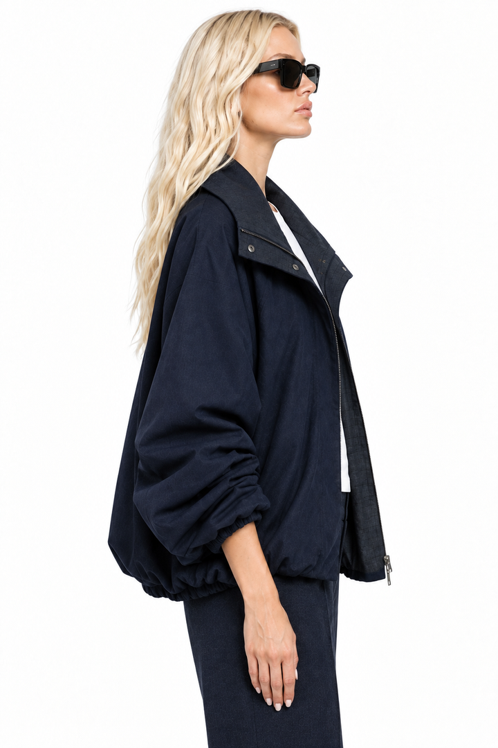 Blonde model wearing navy funnel-neck bomber jacket, side view