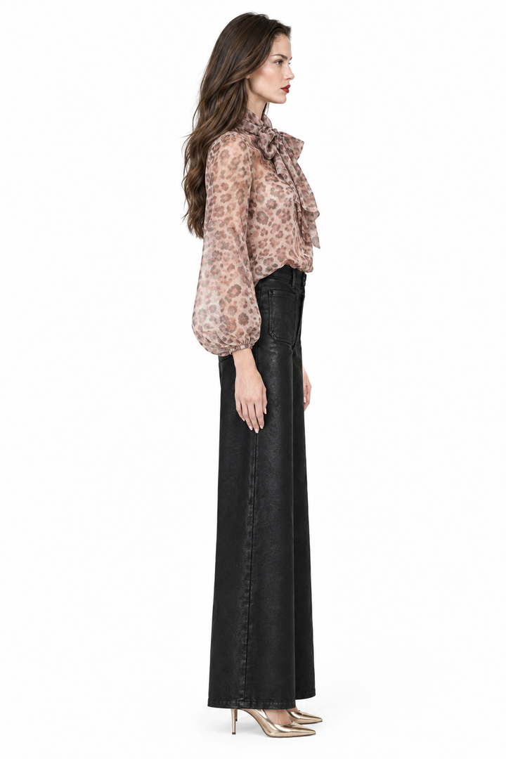 Sloane wearing black coated wide-leg jeans with printed bow blouse and gold pumps, side profile