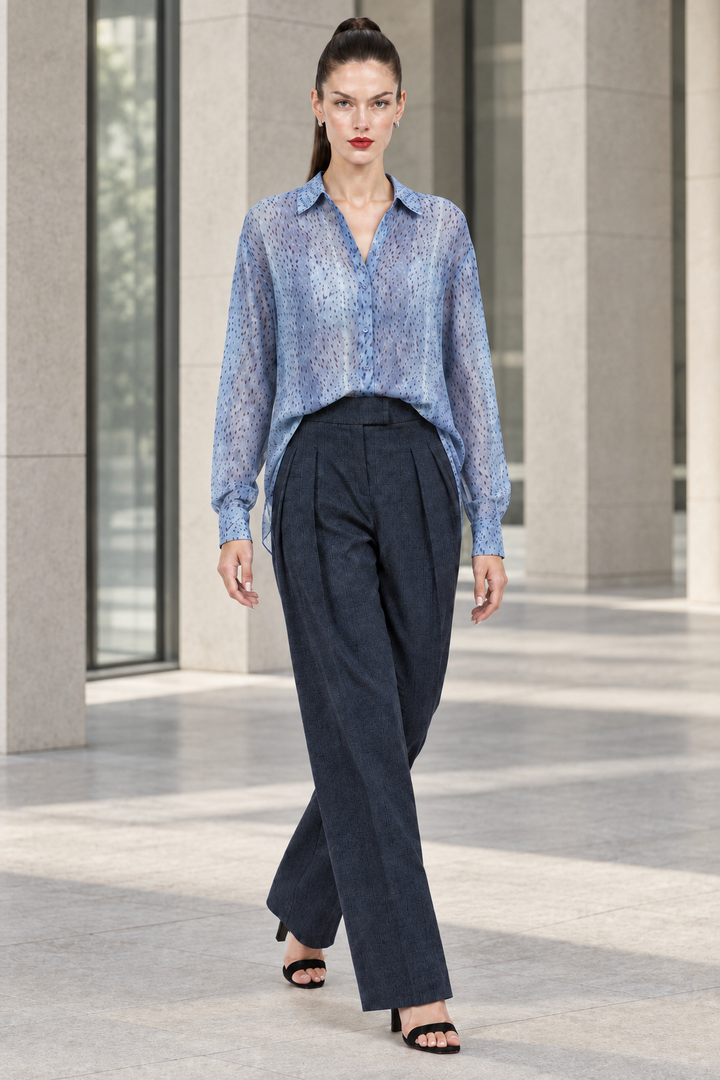 Sloane wearing navy pleated plaid straight-leg trousers and blue printed blouse in a modern architectural setting