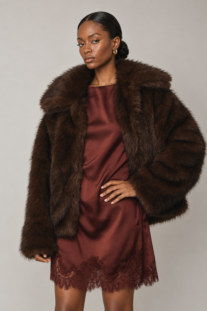 Beciga model wearing chocolate wide-lapel faux-fur jacket over burgundy satin dress, front view