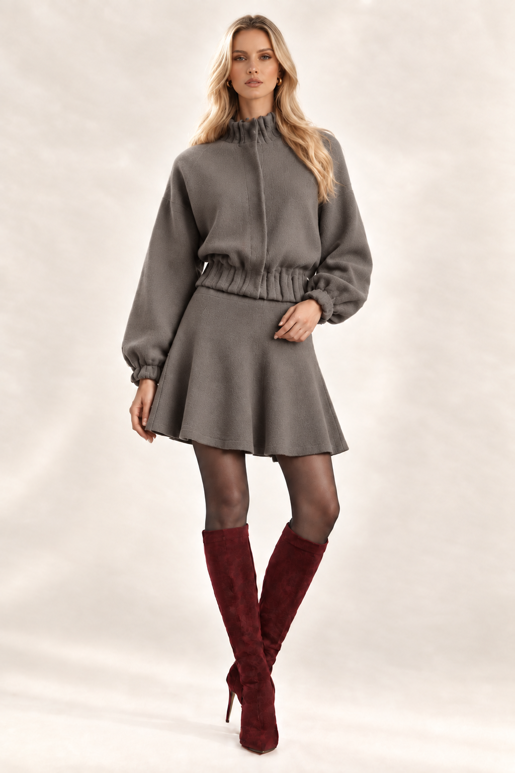 Maggie front view in solid Dark Stone knit flare bottom skirt and matching jacket, sheer charcoal tights and wine knee-high boots