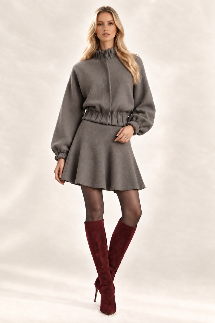 Maggie front view in solid Dark Stone knit flare bottom skirt and matching jacket, sheer charcoal tights and wine knee-high boots